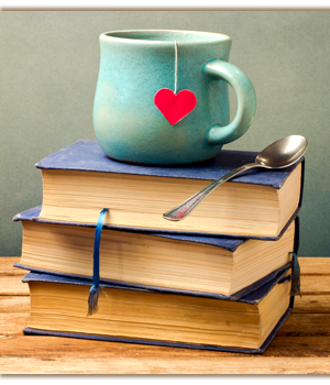 Cup with a heart shaped tea bag string and a spoon on top of stacked books